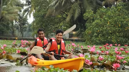 Kerala Kayaking activity -Two boys kayaking through the tranquil backwaters of Alleppey, surrounded by lush green vegetation and traditional Kerala houseboats.